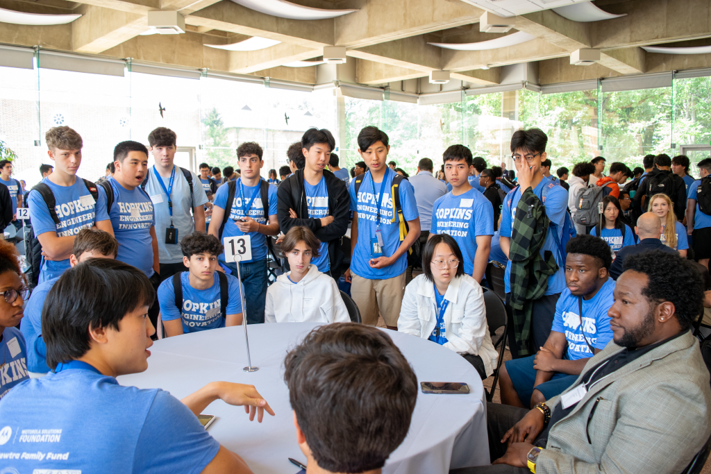 students seated and standing around a table and networking with a professional