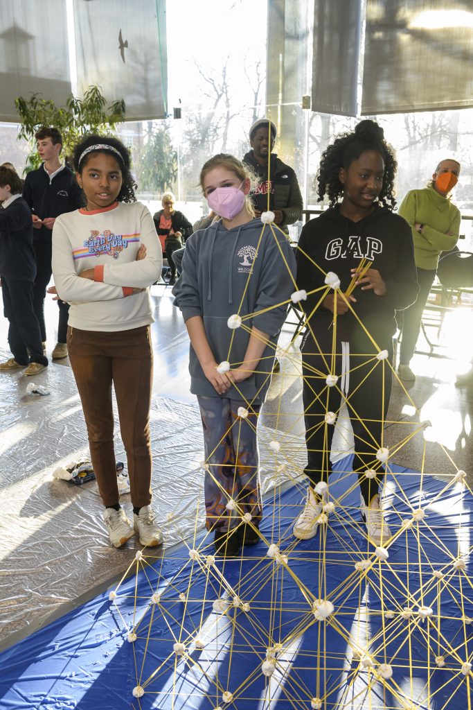 student competitors standing behind a tall towered structure they built using spaghetti pasta noodles and marshmallows